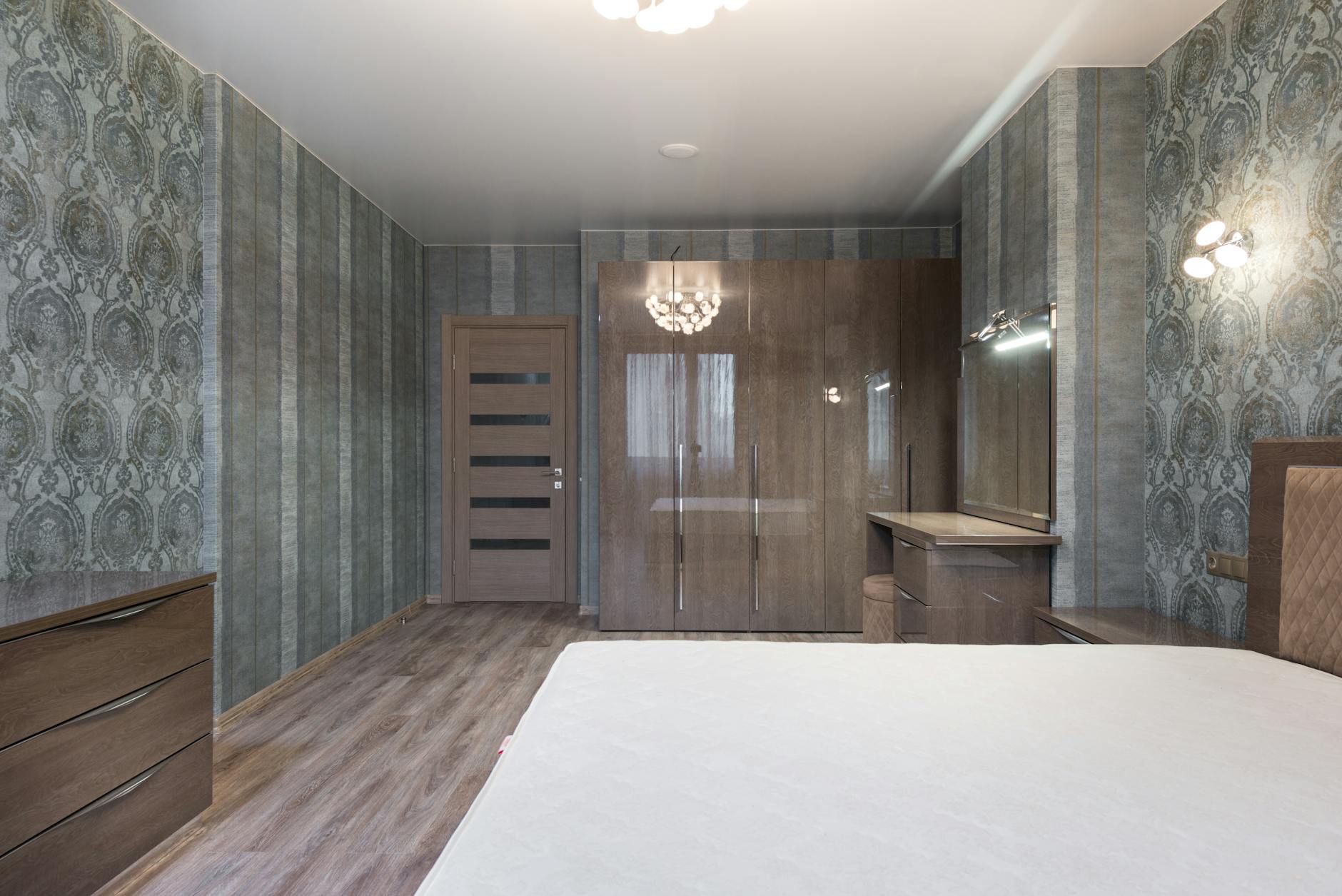 Przestronna sypialnia z łóżkiem i połyskującą szafą z drewnianymi szufladami